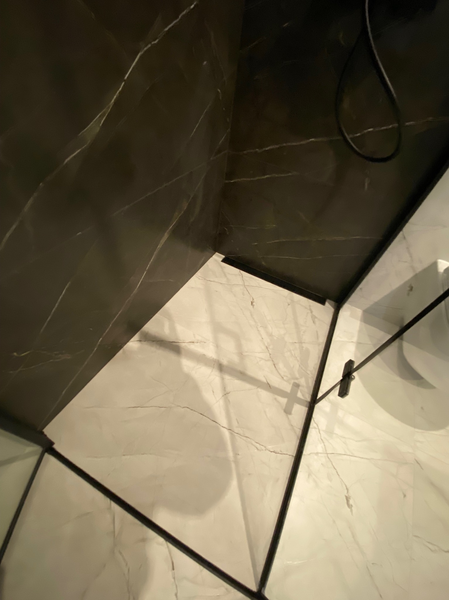 Kabina prysznicowa z czarnymi ramami i odpływem liniowym, wykończona płytkami imitującymi marmur w kolorach czerni i bieli, zrealizowana we Wtórku.