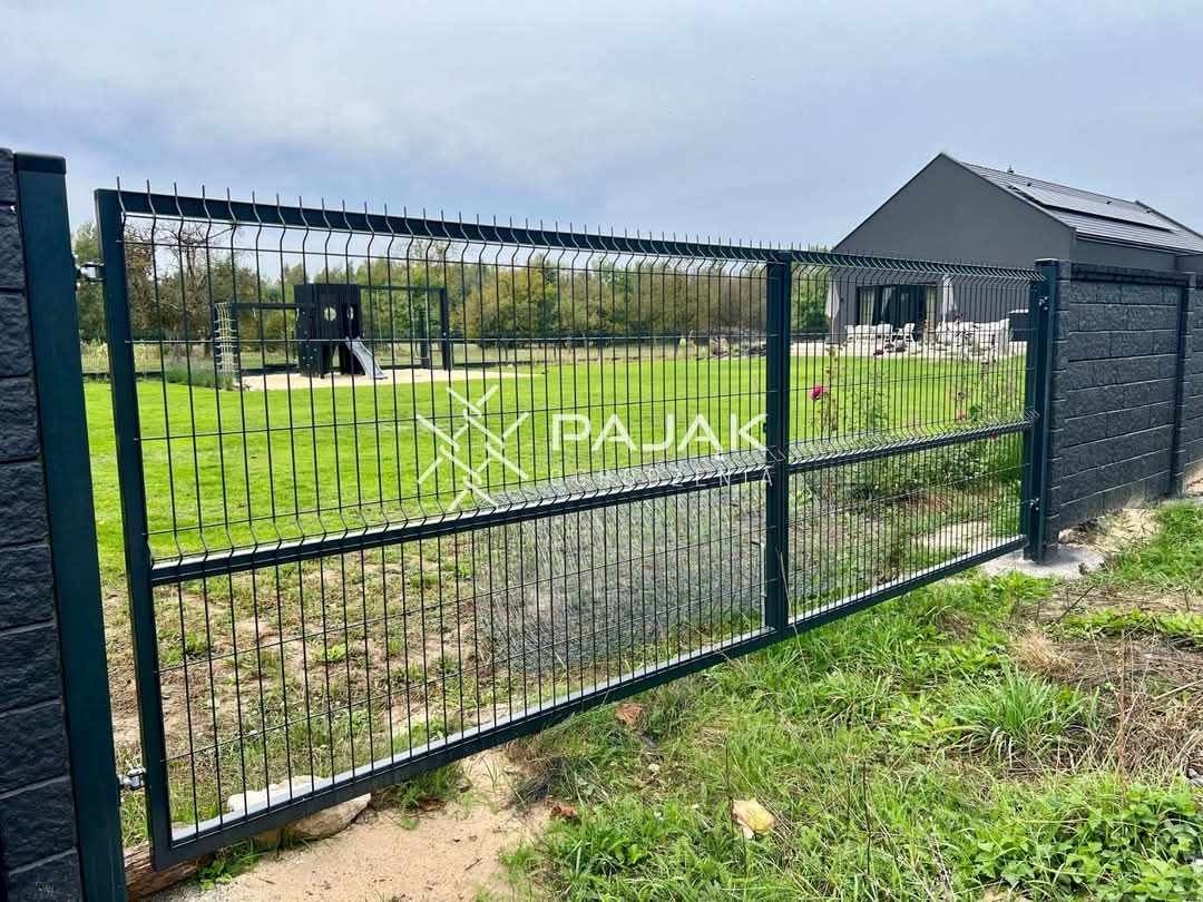 Nowoczesne, grafitowe ogrodzenie z siatki panelowej z widocznym logo firmy na tle zadbanego ogrodu i domu.