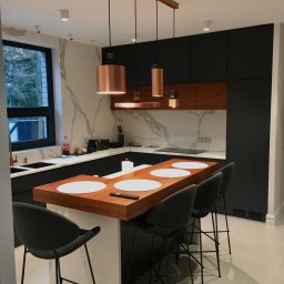 Pracownia m2 - Nowoczesna kuchnia z wyspą, czarne szafki, drewniane akcenty, marmurowy backsplash i miedziane lampy wiszące nad blatem z hokerami.