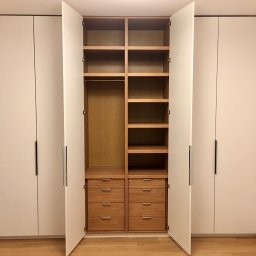 Pracownia m2 - Biała szafa wnękowa z drewnianym wnętrzem i szufladami, otwarte drzwi ukazują półki i drążek na ubrania.