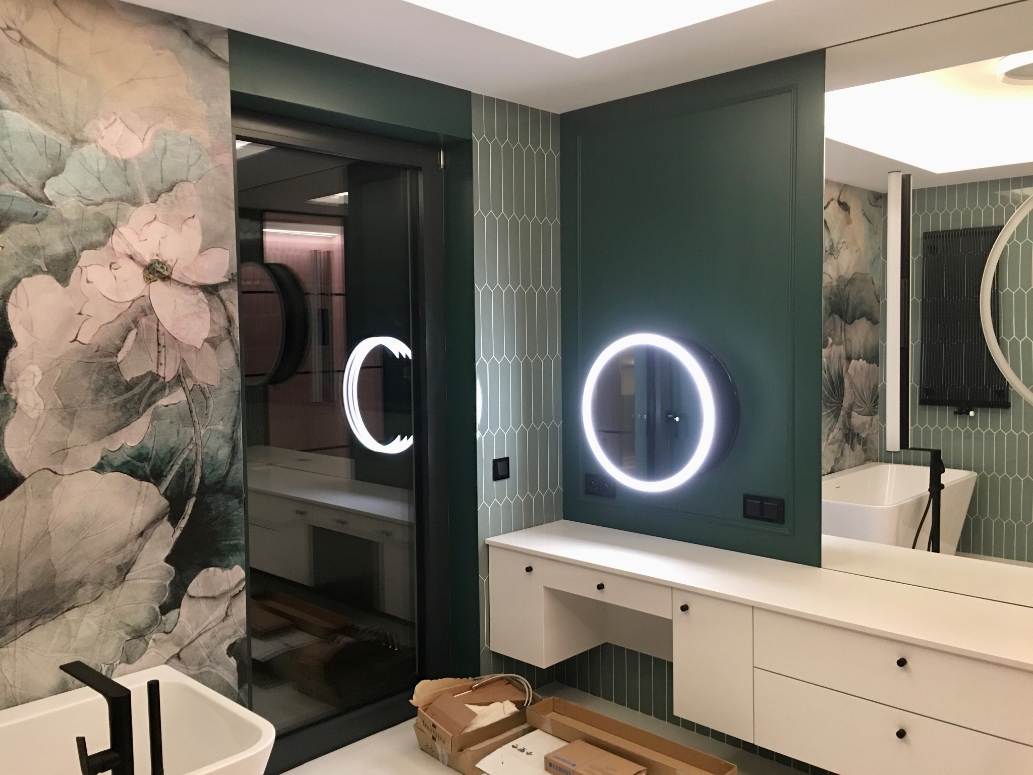 Nowoczesna łazienka w Warszawie z szafką pod umywalkę, okrągłym lustrem z podświetleniem LED i dekoracyjną fototapetą z motywem kwiatowym za szklanymi drzwiami.