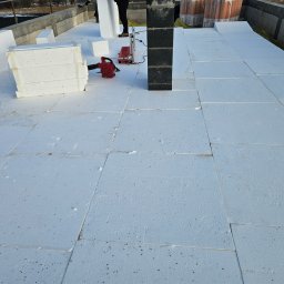 Zarzycki-System Paweł Zarzycki - Układanie białych płyt styropianowych na dachu, widoczny komin, dmuchawa do czyszczenia i fragment osoby w tle.