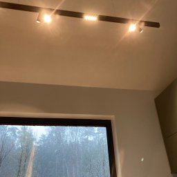 Rafał Potok - Nowoczesna listwa oświetleniowa z reflektorami punktowymi, zamontowana na suficie w jasnym pomieszczeniu z oknem, za którym widać zalesiony krajobraz w zimowej aurze.