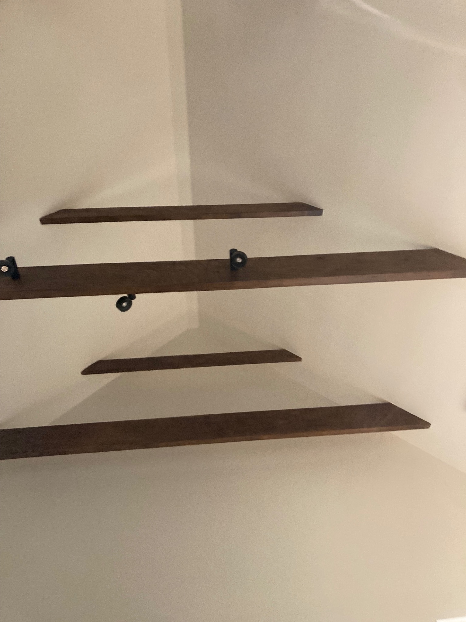 Zamontowane, drewniane półki na ścianie w jasnym pokoju, widoczne czarne uchwyty mocujące.