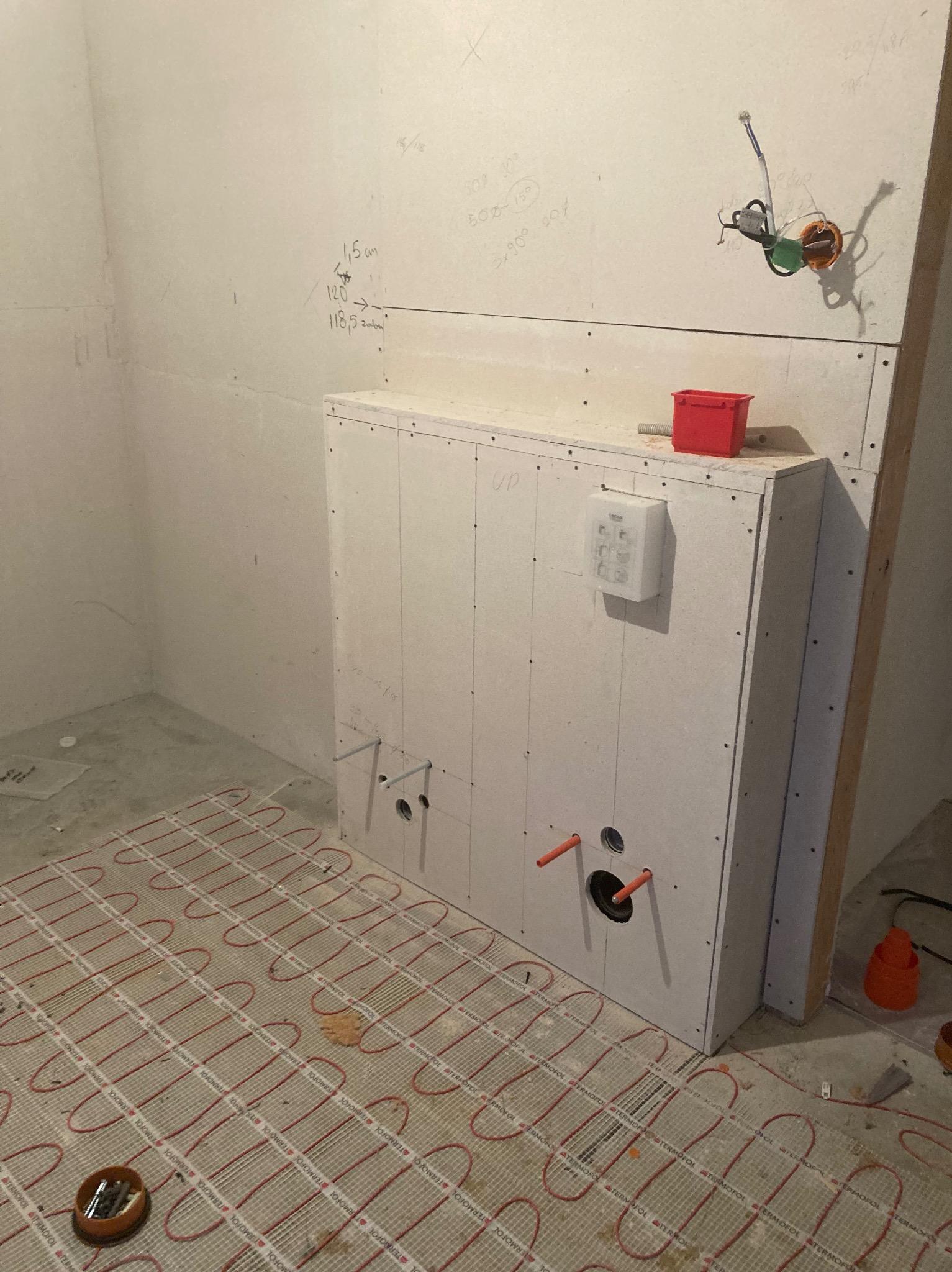 Łazienka w trakcie prac wykończeniowych: zabudowa stelaża WC z płyty karton-gips z widocznymi przyłączami wodno-kanalizacyjnymi, ogrzewanie podłogowe ułożone na posadzce, na ścianie widoczne...