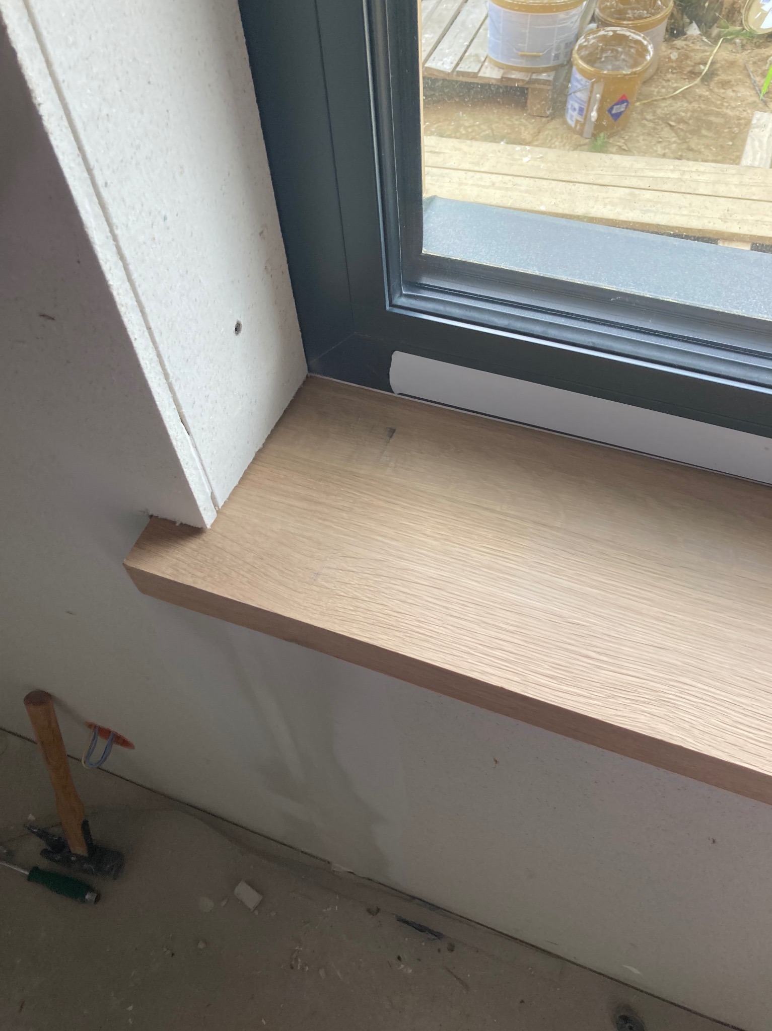 Wnętrze z zamontowanym drewnianym parapetem okiennym, widoczna izolacja termiczna wokół okna oraz narzędzia na podłodze, sugerujące trwający remont.