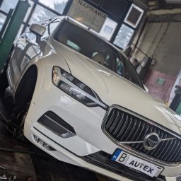 AUTEX Warsztat Samochodowy -Regeneracja Maglownicy Białystok - Białe auto marki Volvo na podnośniku w warsztacie, brak przedniego koła, widoczny numer rejestracyjny z naklejką AUTEX
