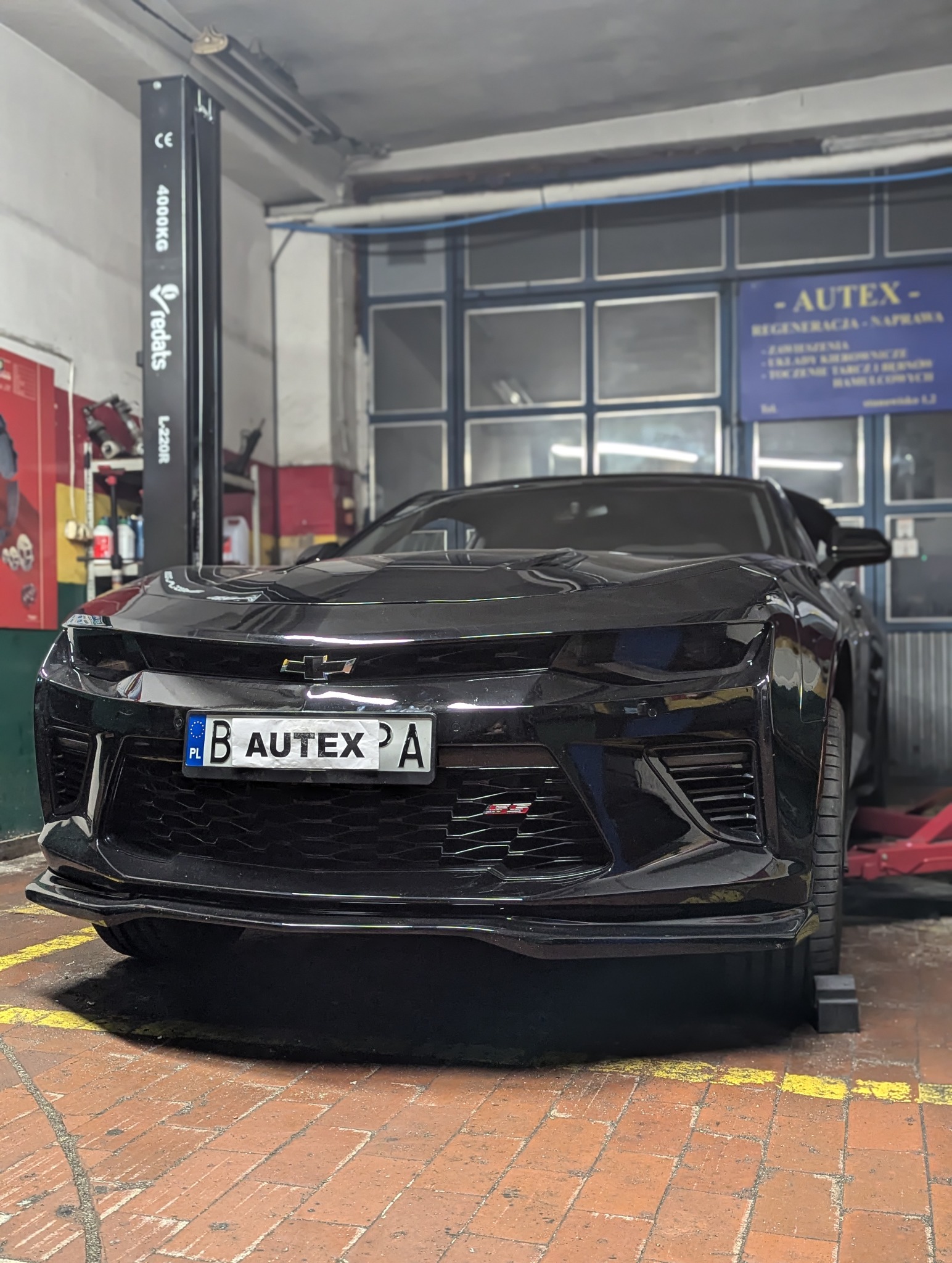 Czarny Chevrolet Camaro z polską tablicą rejestracyjną 'B AUTEX A' stoi w warsztacie samochodowym, widoczny podnośnik kolumnowy i szyld warsztatu Autex.