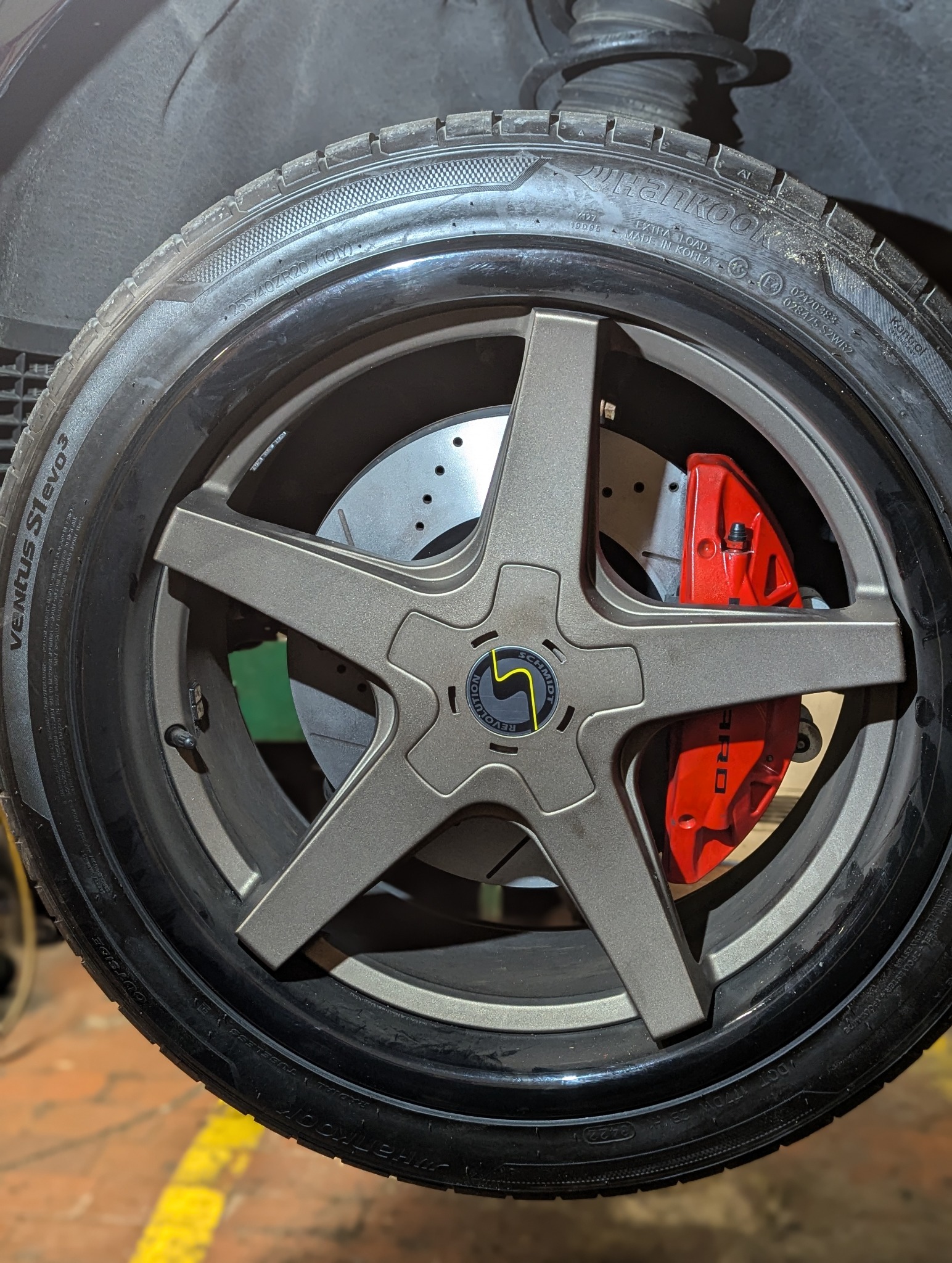 Szare felgi aluminiowe z pięcioramienną gwiazdą, czerwony zacisk hamulcowy ARO, opona Hankook Ventus S1 evo3, widoczne tarcze hamulcowe z nawierceniami.