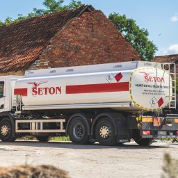SETON CICHOCKI MATUSIEWICZ SPÓŁKA KOMANDYTOWA - Cysterna z logo firmy Seton, dostarczająca paliwa płynne, zaparkowana na betonowym placu przed ceglanym budynkiem, widoczny pracownik podczas tankowania.