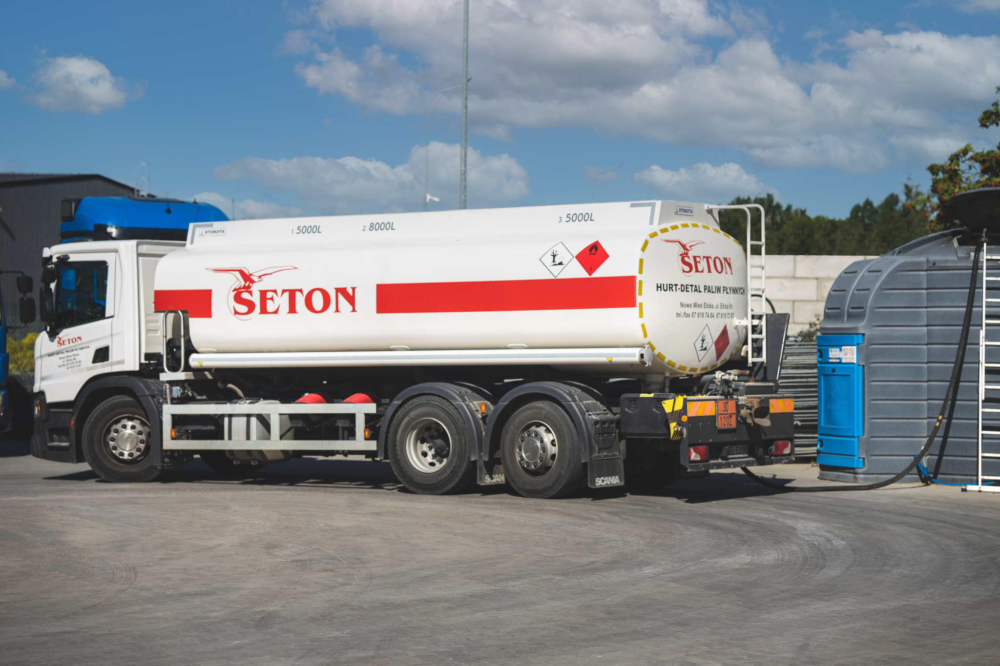 Cysterna paliwowa firmy Seton podłączona wężem do zbiornika dystrybucyjnego na zewnątrz, widoczne oznaczenia ADR.