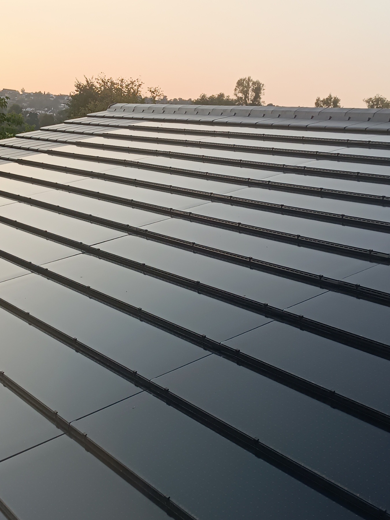 Błyszczące, ciemnoszare dachówki ceramiczne ułożone rzędami na nowym dachu, widok z góry przy zachodzącym słońcu.