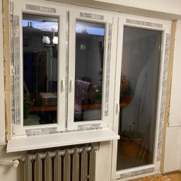 White Energy Przemysław Lis Okna Pro + - Montaż okna PCV Salamander, widoczne taśmy zabezpieczające na ramie, stary grzejnik pod oknem i fragment parkietu.