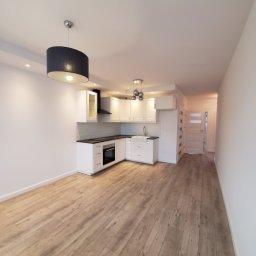 Presko - Jasne, przestronne wnętrze po remoncie: biała zabudowa kuchenna z czarnym blatem i okapem, drewniana podłoga, nowoczesne lampy wiszące.