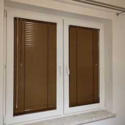 PAMI SPÓŁKA Z OGRANICZONĄ ODPOWIEDZIALNOŚCIĄ - Brązowe poziome lamele w białej ramie okiennej, widok z bliska na zamknięte osłony okienne w nowym budownictwie.