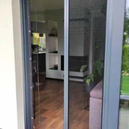 Zastosowanie pionowej siatki przeciw owadom w drzwiach tarasowych w Spiczynie, widok na wnętrze domu z drewnianą podłogą i elementami dekoracyjnymi.