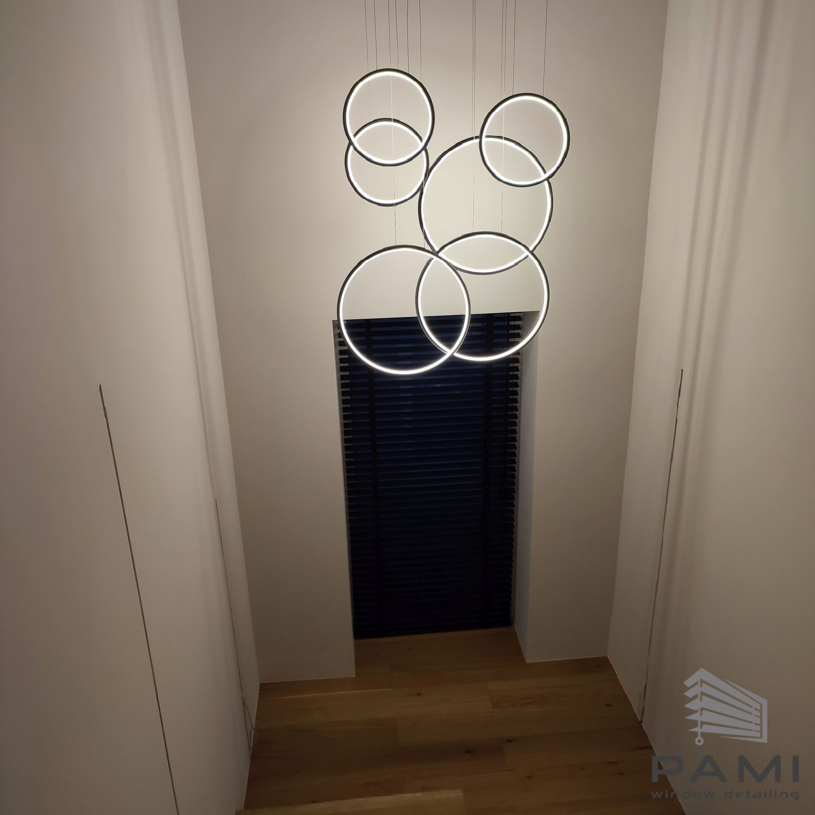 Wnętrze z ciemnymi żaluzjami w oknie na końcu schodów, oświetlone nowoczesną lampą z okręgów.