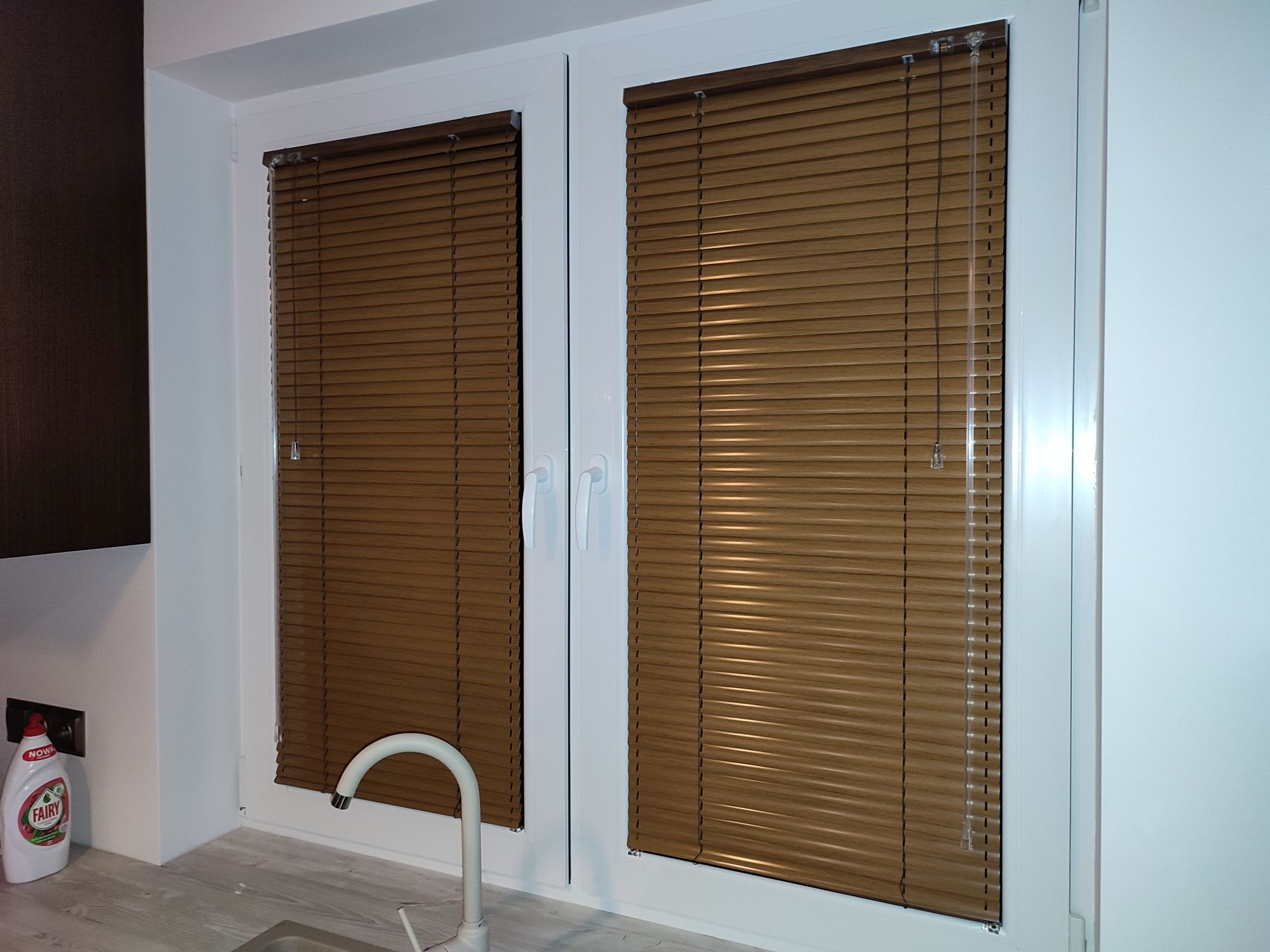 Brązowe listkowe przesłony okienne w kuchni, widoczne na tle zlewu i płynu do naczyń.