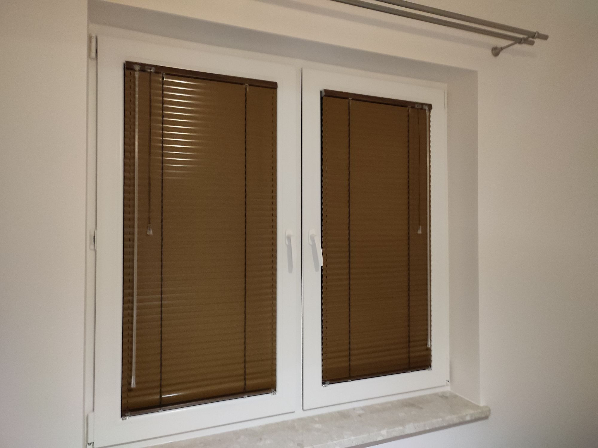 Brązowe poziome lamele w białej ramie okiennej, widok z bliska na zamknięte osłony okienne w nowym budownictwie.