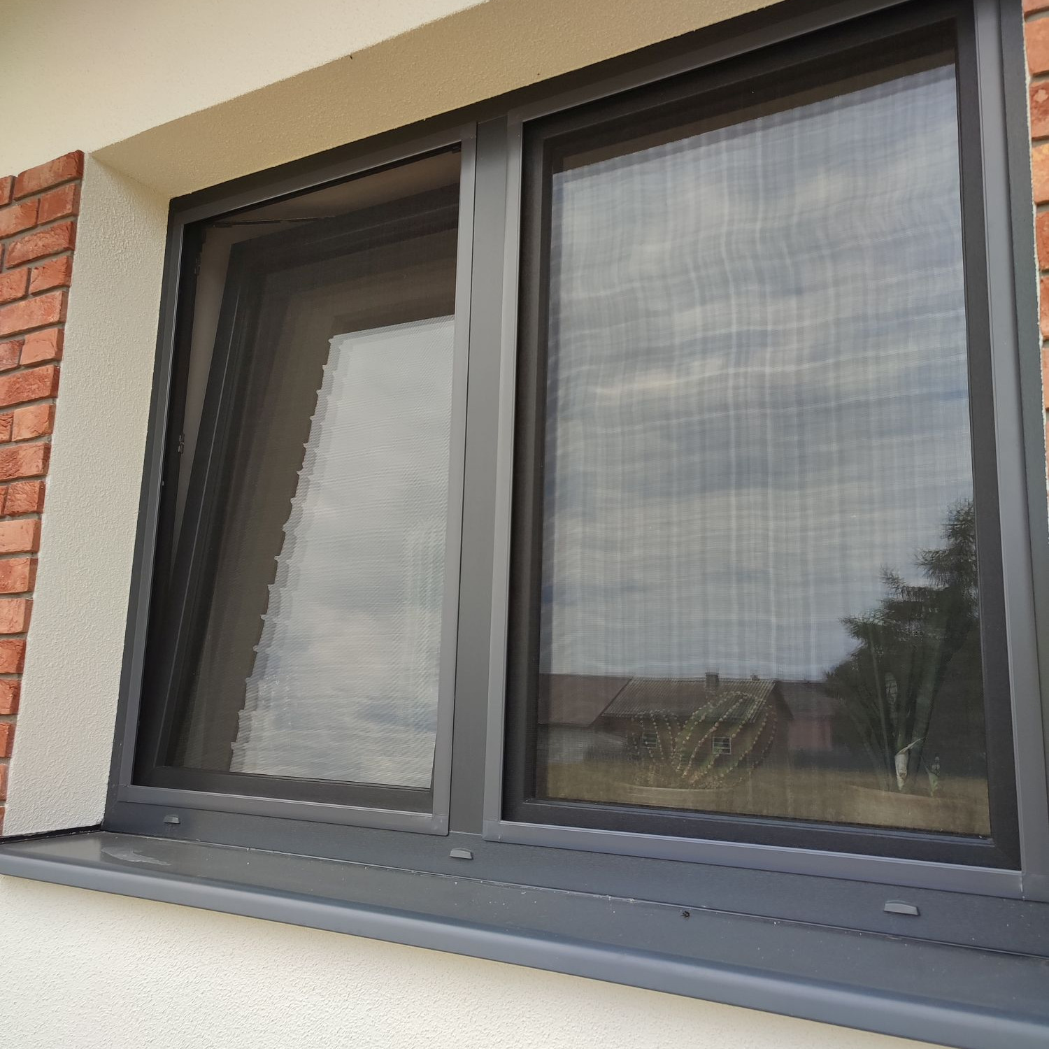 Szczegółowe ujęcie okna z zamontowaną siatką przeciw owadom w Spiczynie, widoczne odbicie otoczenia w szybie.