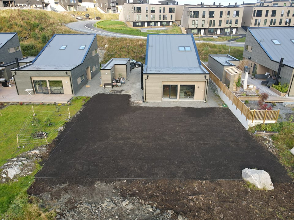 Przygotowany teren pod trawnik z widocznymi granicami, w tle nowoczesne domy w zabudowie szeregowej na wzgórzu.