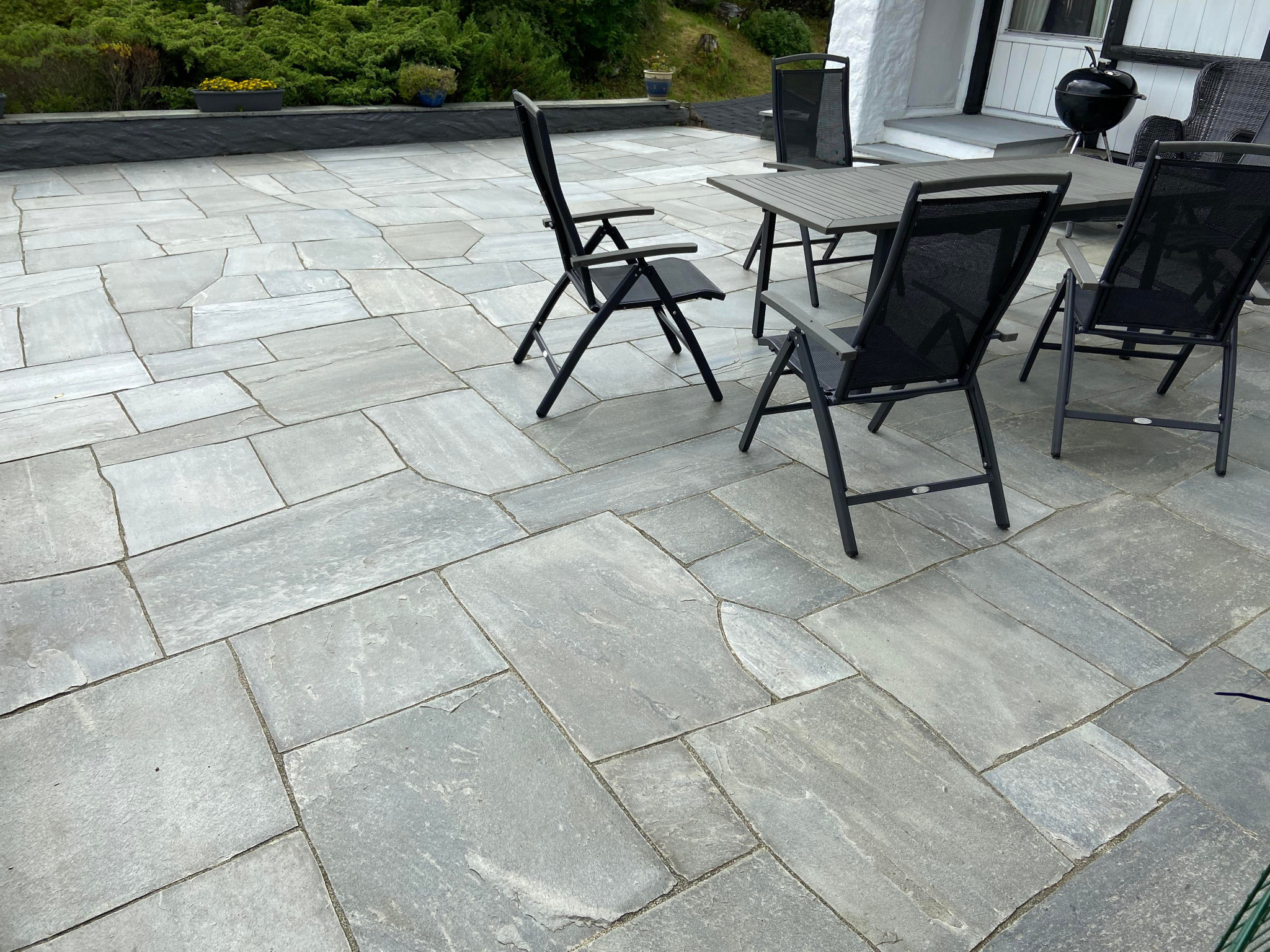 Ułożona szara kostka brukowa na tarasie z kompletem mebli ogrodowych i grillem w tle.