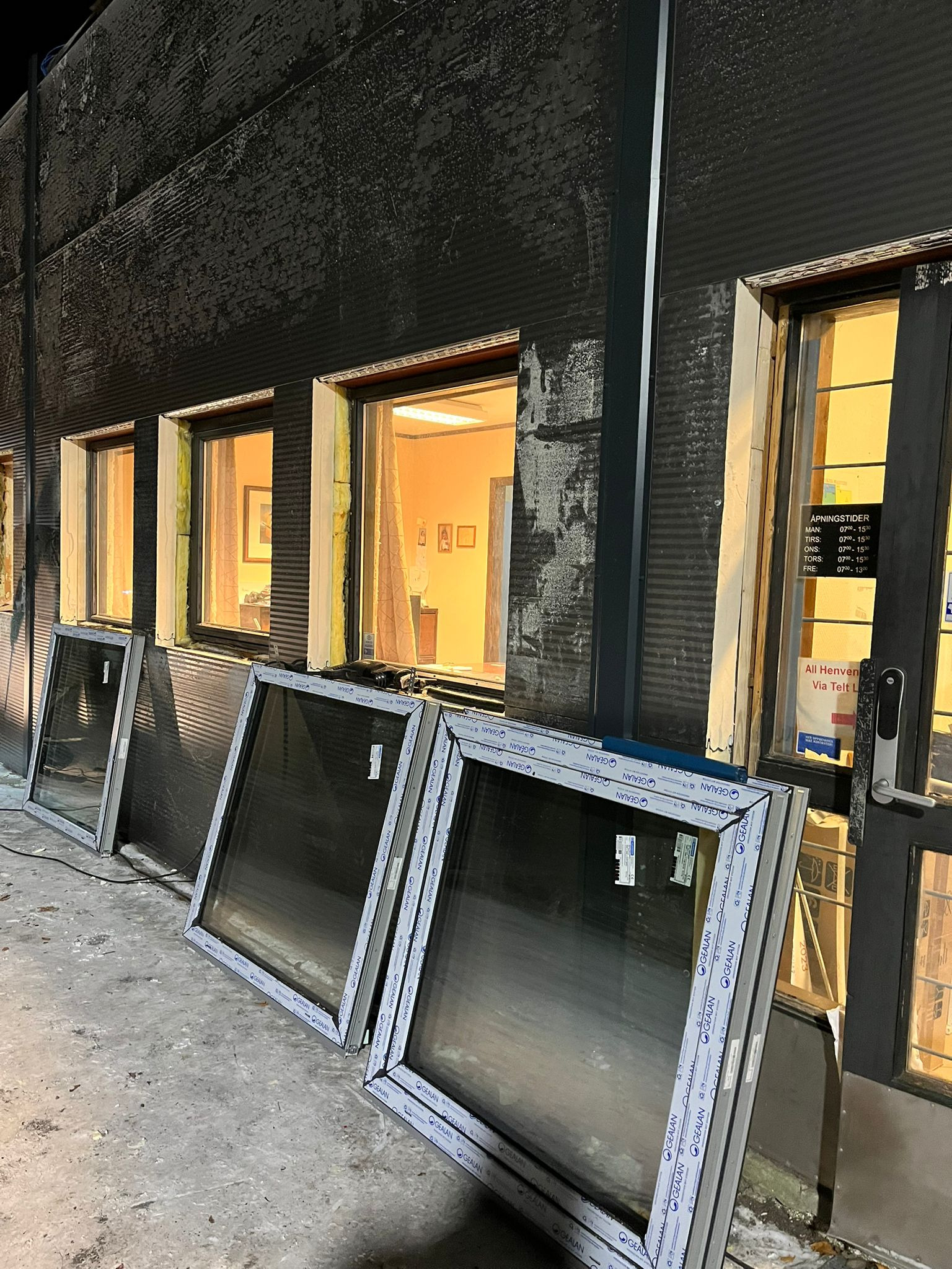 Przygotowane do montażu okna PCV z widocznym profilem Gealan, opierają się o fasadę budynku z widoczną izolacją wokół zamontowanych okien. W tle widoczne wnętrze budynku.