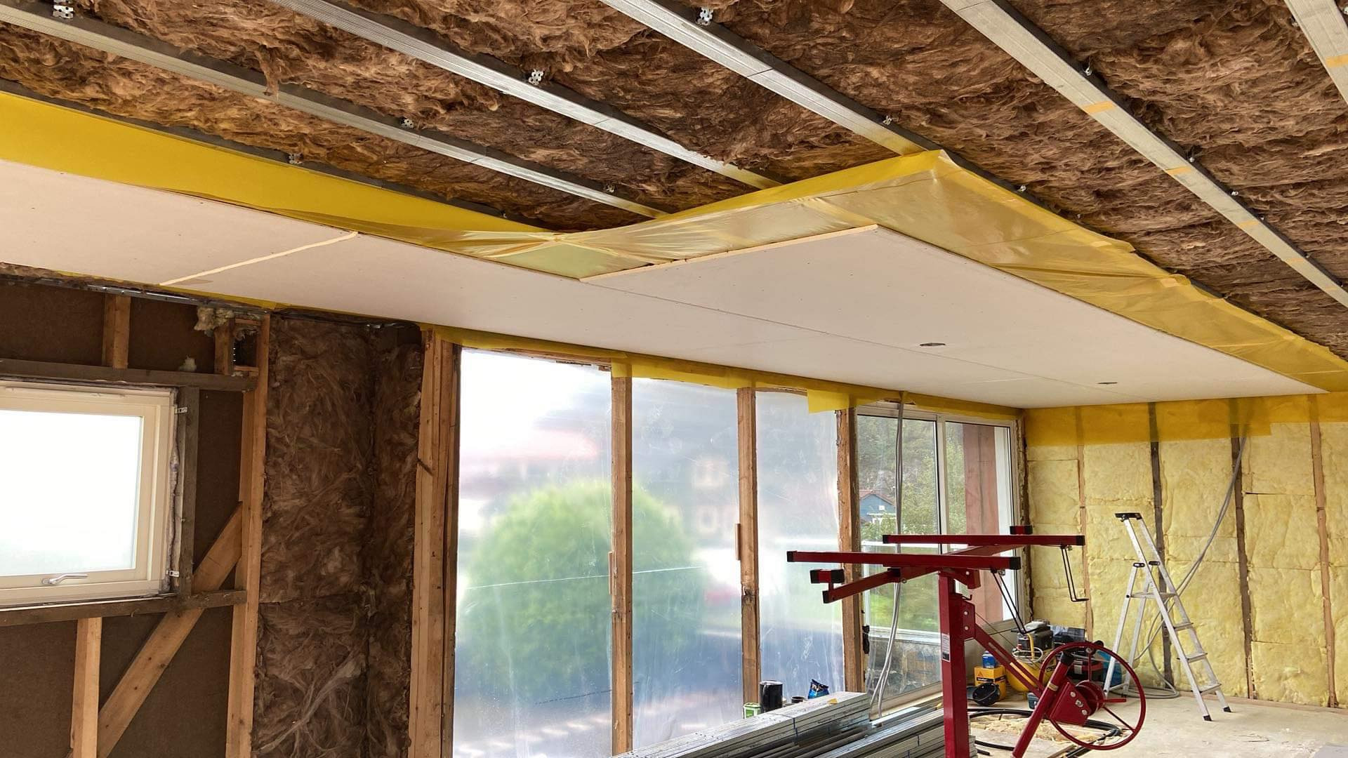 Montaż sufitu podwieszanego z płyt karton-gips w trakcie prac wykończeniowych, widoczne profile, izolacja wełną mineralną oraz podnośnik do płyt.