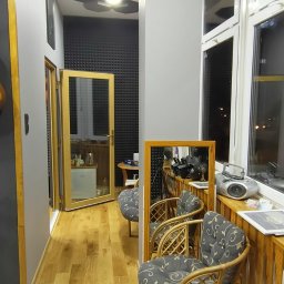 SINGERTON TOMASZ ŚPIEWAK - Wnętrze studia nagrań z panelami akustycznymi na ścianie, drewnianą podłogą i wiklinowymi fotelami z szarymi poduszkami w kwiaty, widok na okno i sprzęt nagraniowy.