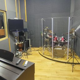 SINGERTON TOMASZ ŚPIEWAK - Wnętrze studia nagrań z pianinem cyfrowym, perkusją Sonor oddzieloną szybą akustyczną, monitorami studyjnymi i panelami akustycznymi na ścianach i suficie.