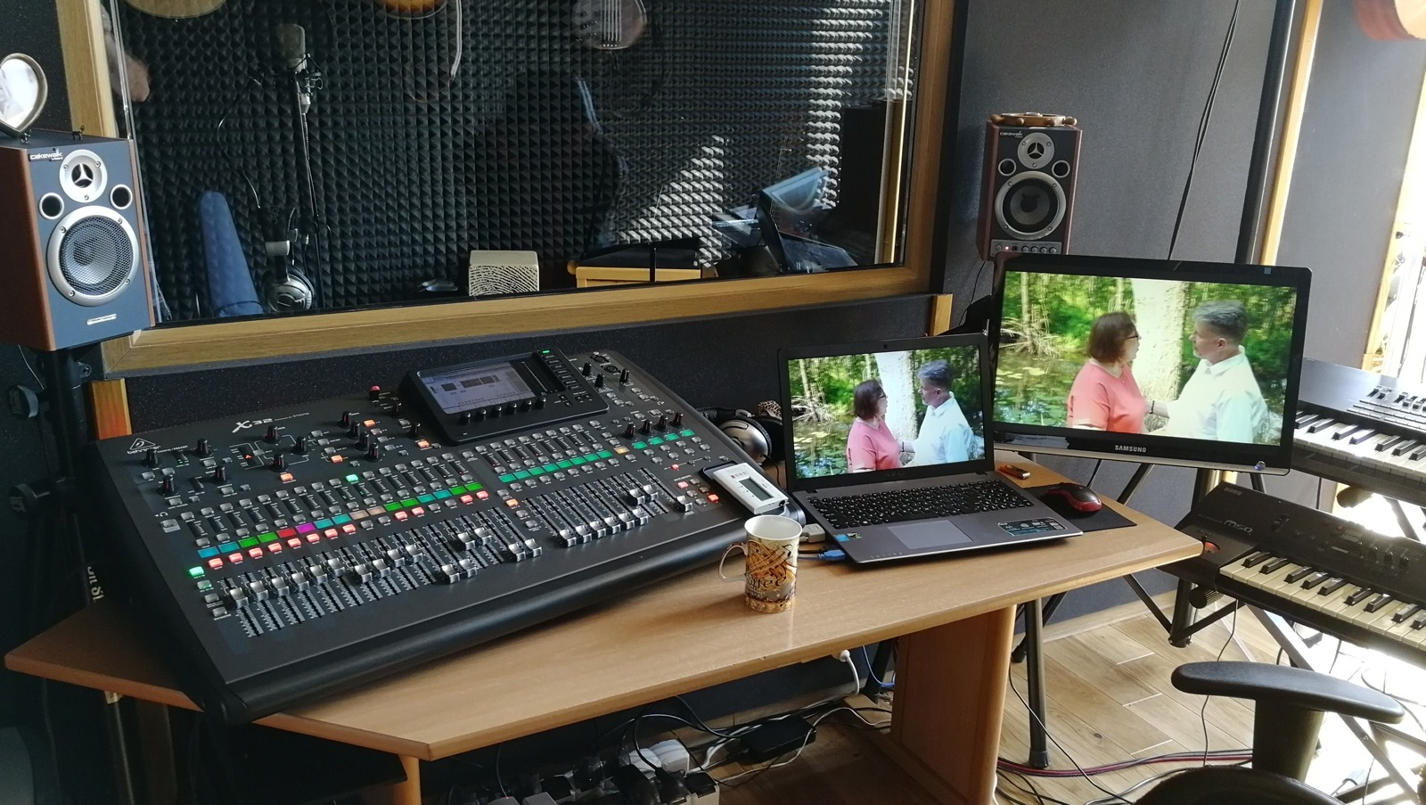 Profesjonalny stół mikserski Behringer X32 w studiu nagrań, obok laptop i monitor wyświetlające scenę z filmu, w tle pianka akustyczna na ścianie i odsłuchy studyjne Cakewalk.