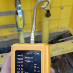 Usługi kominiarsko-Gazowe Aleksander Ostrowski - Żółty detektor gazu z elastyczną sondą, wskazujący obecność metanu i propanu, na tle żółtej instalacji gazowej.