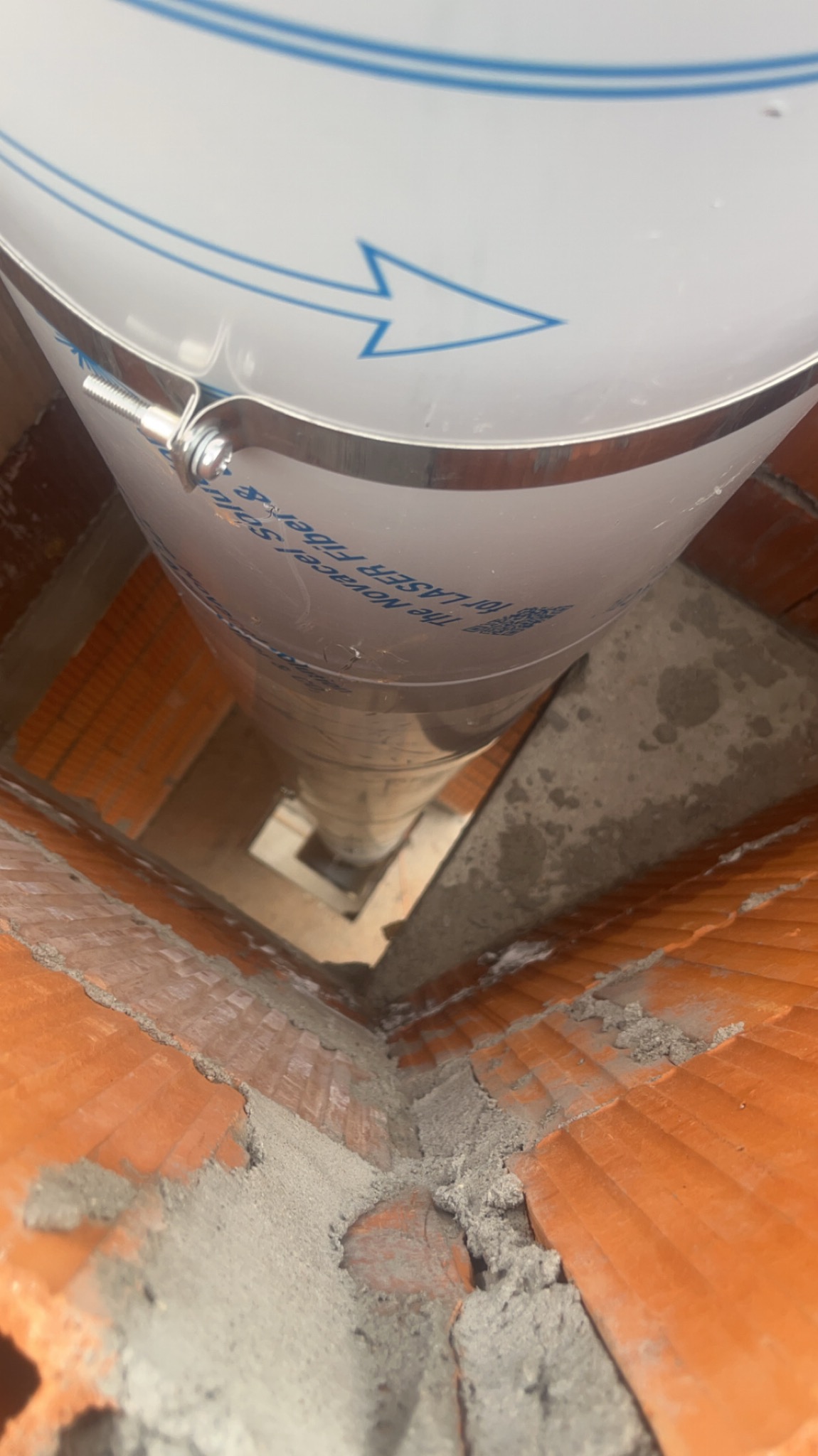 Wnętrze komina z wkładem ze stali nierdzewnej, widok z góry. Wkład zabezpieczony obejmą z napisem. Ceglana konstrukcja komina z zaprawą.