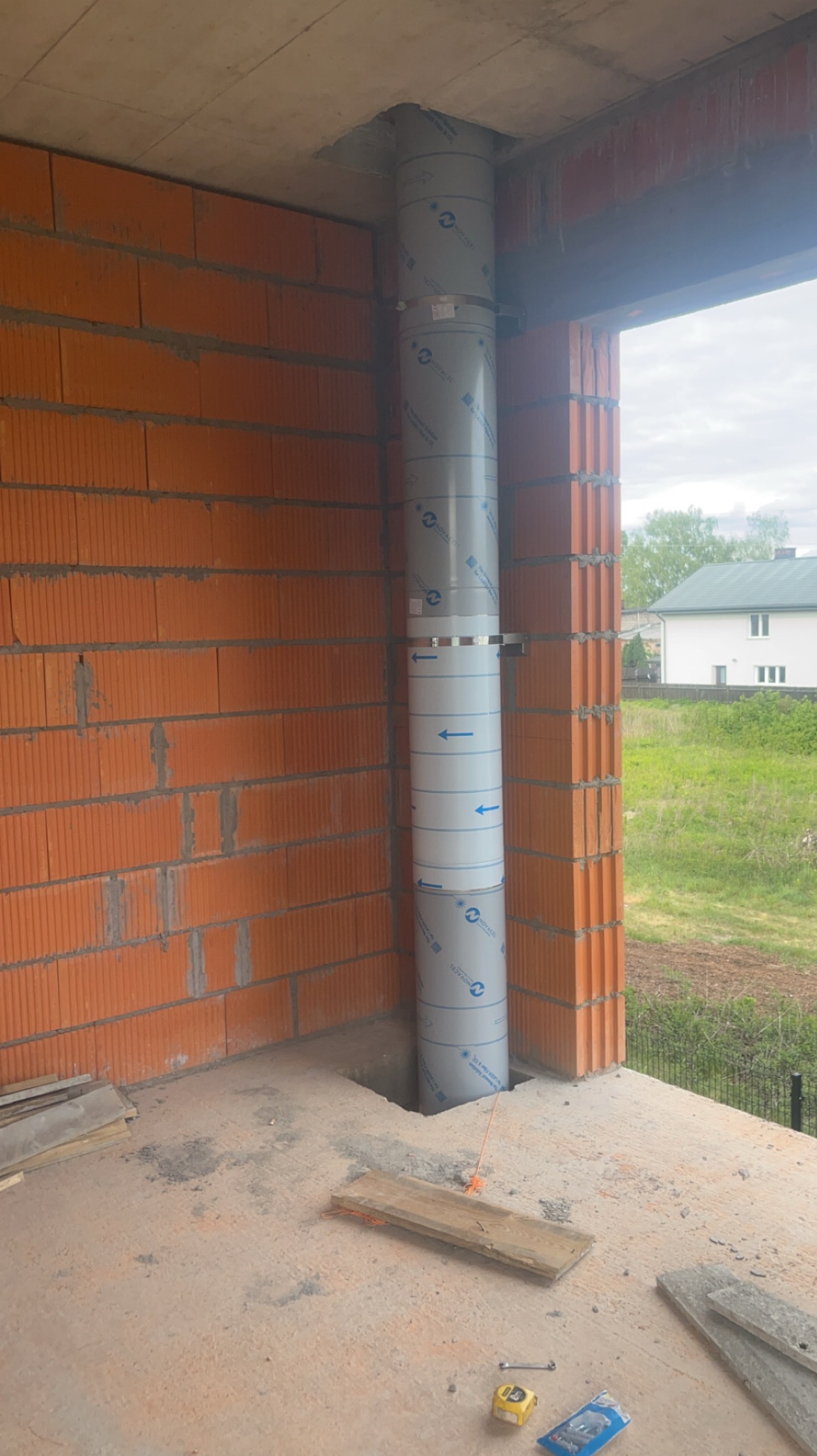 Montaż pionowego, segmentowego przewodu kominowego z blachy w surowym stanie budynku, widoczne cegły i elementy konstrukcyjne.