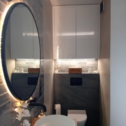 MAFF - Nowoczesna łazienka z owalnym lustrem podświetlanym LED, umywalką nablatową, czarną armaturą i wiszącą szafką z oświetleniem punktowym.