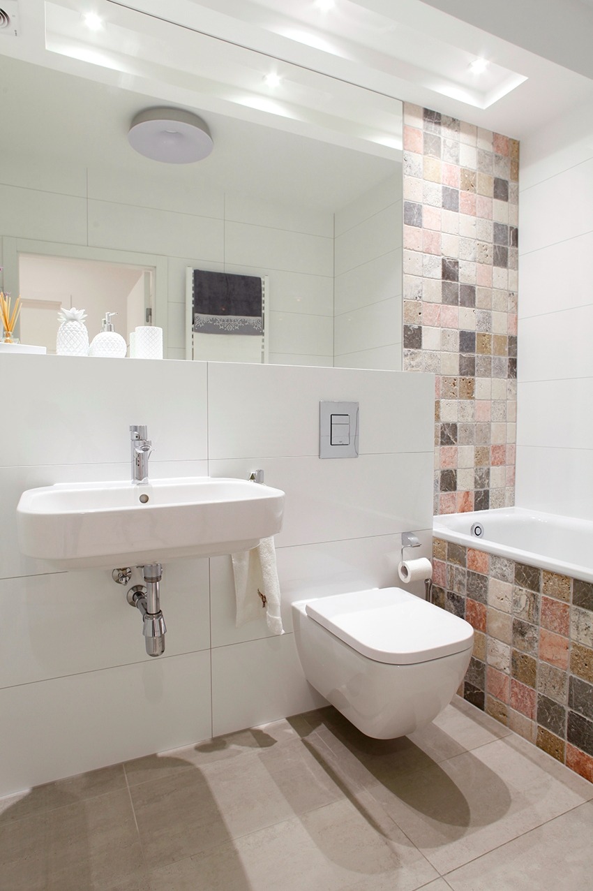 Nowoczesna łazienka z podwieszaną toaletą, umywalką nablatową i mozaiką w odcieniach beżu i brązu, odbicie w lustrze ukazuje dekoracyjne akcenty.