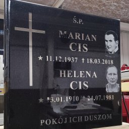 Kamieniarstwo GAP - Czarny, polerowany pomnik z wygrawerowanymi srebrnymi literami, krzyżem i portretami, ustawiony na drewnianej podstawie w warsztacie kamieniarskim.