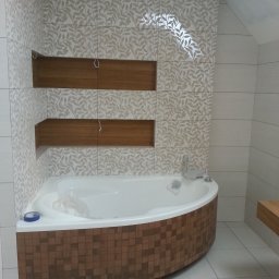 Kraszbud - Nowoczesna łazienka z wanną obudowaną mozaiką w odcieniach brązu, ściany wyłożone płytkami z motywem liści, w ścianie wnęki wykończone drewnem, widoczne niedokończone podłączenie elektryczne.