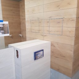 Kraszbud - Montaż płytek imitujących drewno w łazience, widoczne otwory inspekcyjne, częściowo zamontowany stelaż podtynkowy Geberit Sigma i zdjęcie referencyjne.
