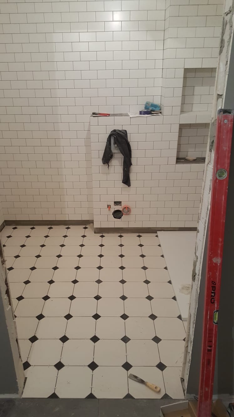 Białe płytki metra na ścianie i biało-czarna podłoga w kratkę w łazience w trakcie remontu, widoczny poziomica i narzędzia.