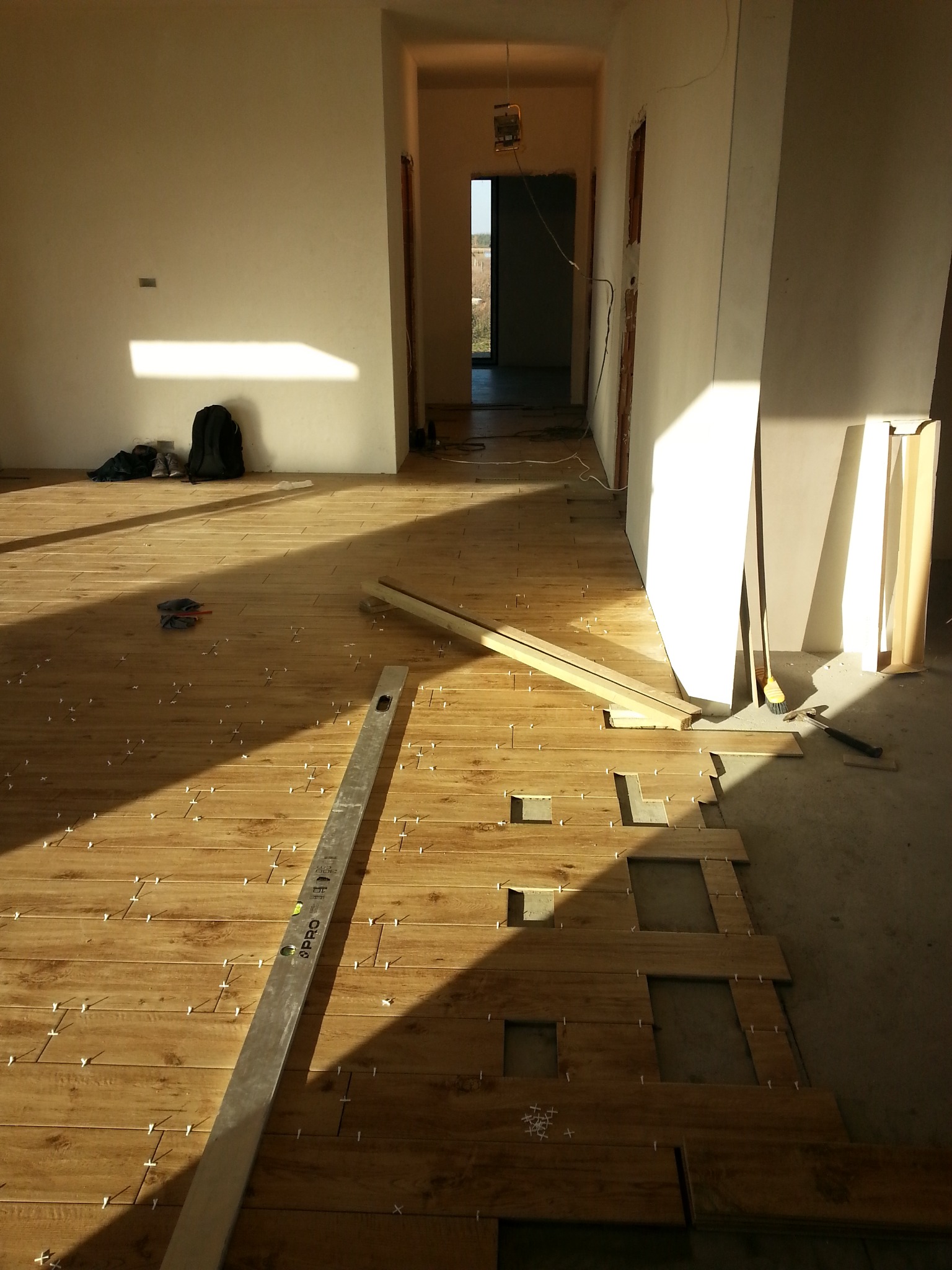 Montaż drewnopodobnych płytek podłogowych w jasnym wnętrzu, widoczny poziomica, krzyżyki dystansowe i częściowo ułożona podłoga.
