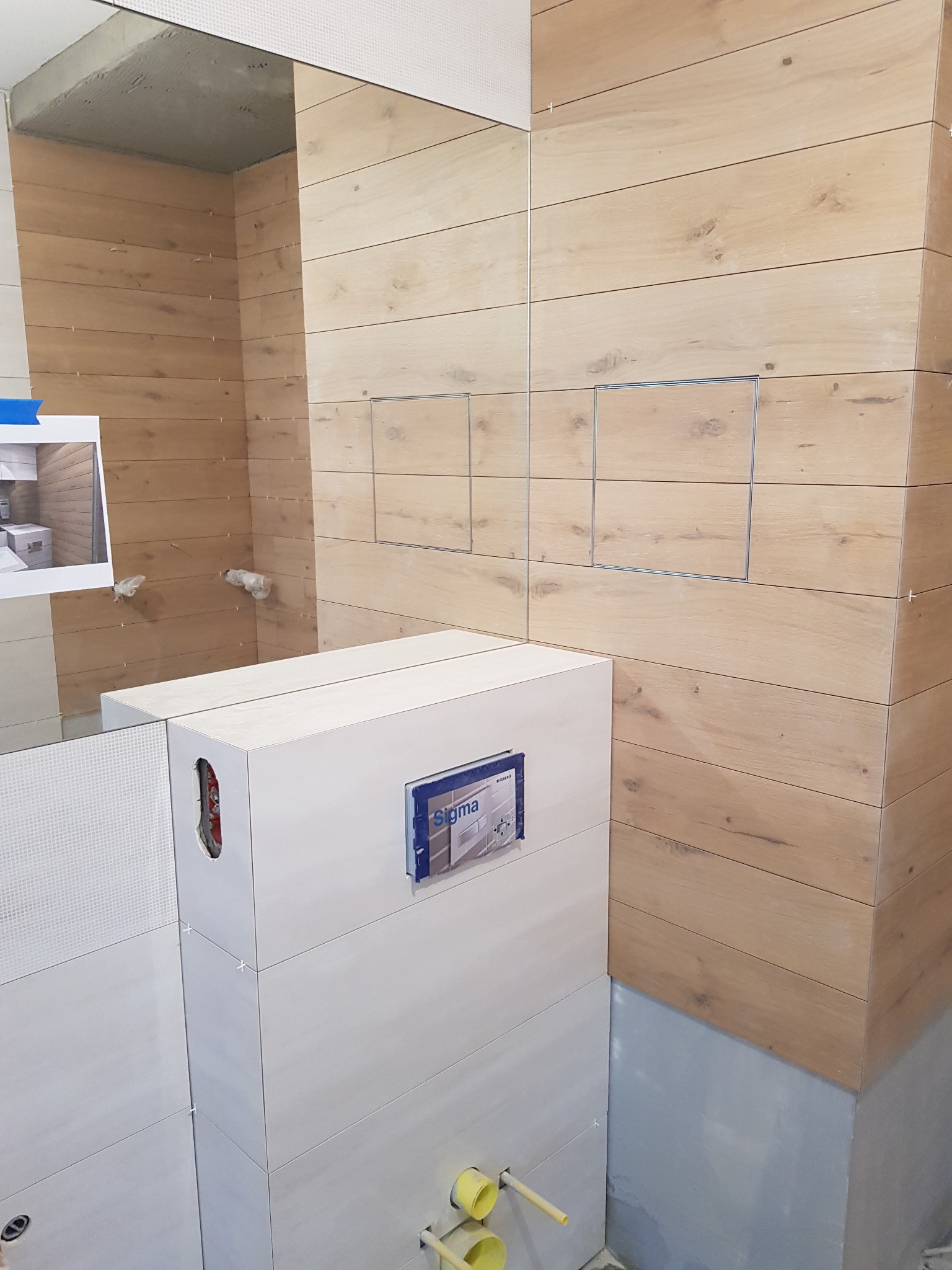 Montaż płytek imitujących drewno w łazience, widoczne otwory inspekcyjne, częściowo zamontowany stelaż podtynkowy Geberit Sigma i zdjęcie referencyjne.