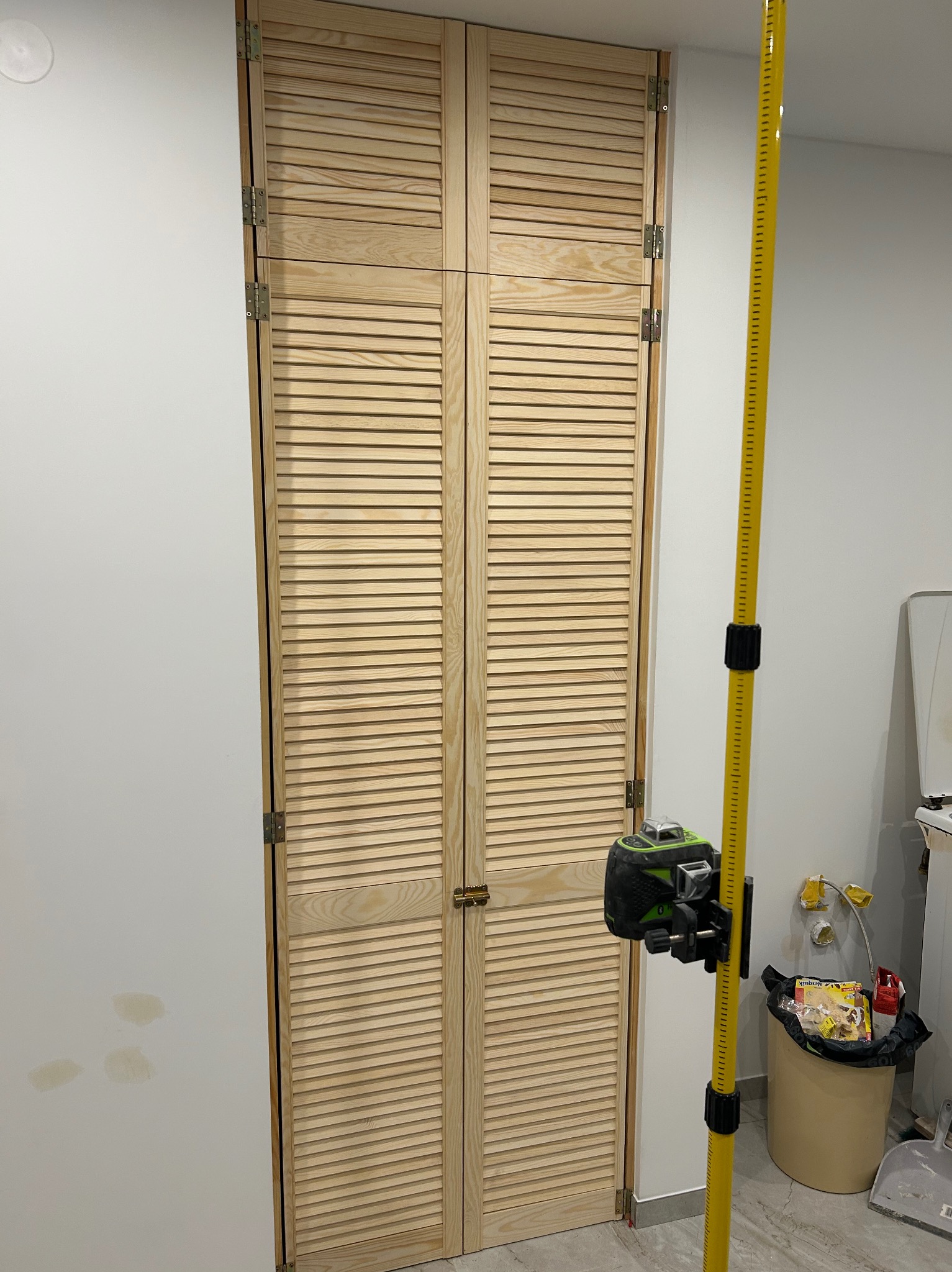 Nowe, drewniane, lamelowe drzwi przesuwne zamontowane w ścianie, sprawdzane poziomnicą laserową; widoczne ślady po szpachlowaniu na ścianie obok.