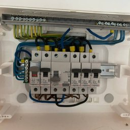 ElektroPakiet - Wewnętrzny widok skrzynki rozdzielczej z zainstalowanymi bezpiecznikami Legrand, widoczne przewody w kolorach niebieskim, czarnym, żółto-zielonym i brązowym.