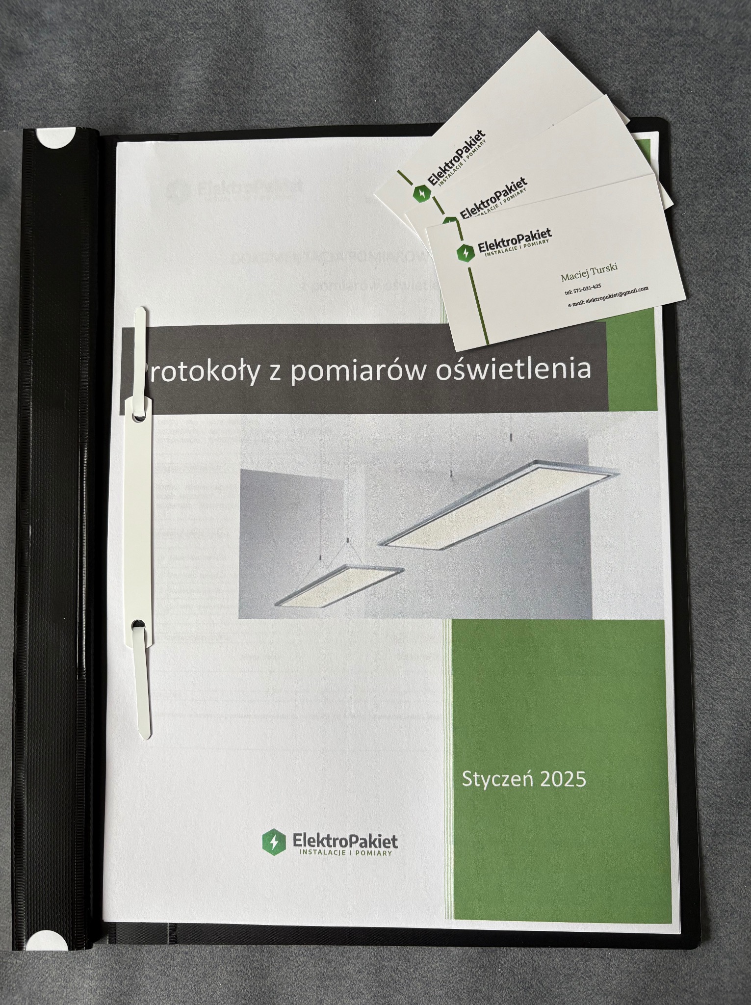 Otwarty segregator z dokumentem 'Protokoły z pomiarów oświetlenia' firmy ElektroPakiet oraz wizytówki Macieja Turskiego, styczeń 2025.