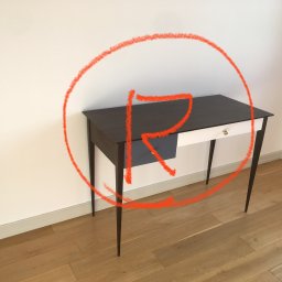 Sztuka Tworzenia Mebli - Minimalistyczny stolik z ciemnym blatem, jasnym frontem szuflady i smukłymi nóżkami, stojący na drewnianej podłodze przy białej ścianie, oznaczony okręgiem z czerwoną literą R.