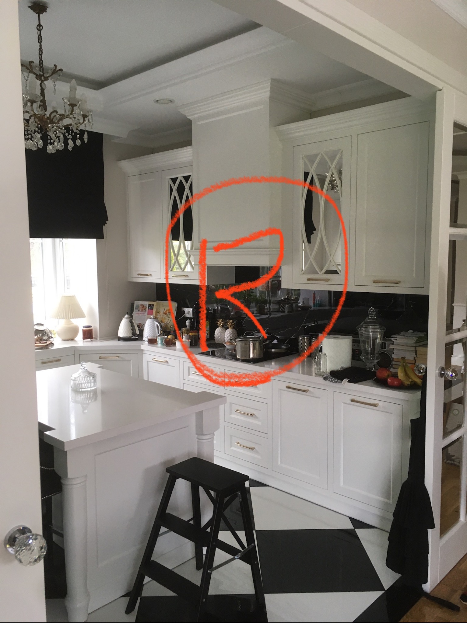 Jasna, przestronna kuchnia w Stanisławowie z białymi szafkami z geometrycznymi przeszkleniami, czarnym blatem i podłogą w szachownicę; widoczny fragment wyspy kuchennej i czarny stołek drabinkowy.