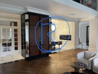 Elegancka szafa wnękowa z lustrzanymi drzwiami i ciemnobrązowymi panelami, wkomponowana w przestronne wnętrze z parkietem w jodełkę i widokiem na dalszą część domu.