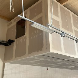 Kacper Siwiec - Wnętrze w trakcie wykańczania: ściany z płyt w systemie suchej zabudowy, widoczne łączenia płyt wymagające dalszej obróbki, podwieszany sufit, białe płytki na ścianie, instalacje elektryczne...