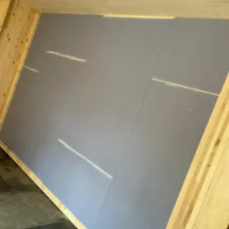 Skośna ściana poddasza z zamontowanymi szarymi płytami, widoczne drewniane elementy konstrukcyjne i łączenia płyt z widocznymi śladami szpachli.